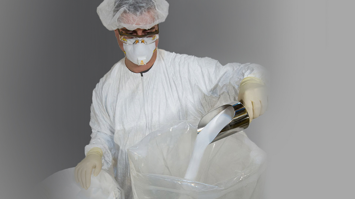 Biomanufacturing professional wearing a mask, hair net, and gloves pours powder into the EZ BioPac® from ILC Dover