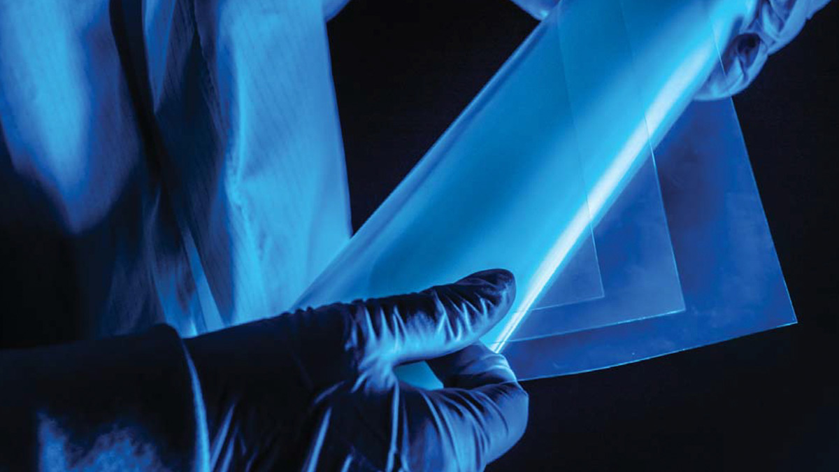 A person wearing gloves handles one ArmorFlex® Film with others lined up on a blue background
