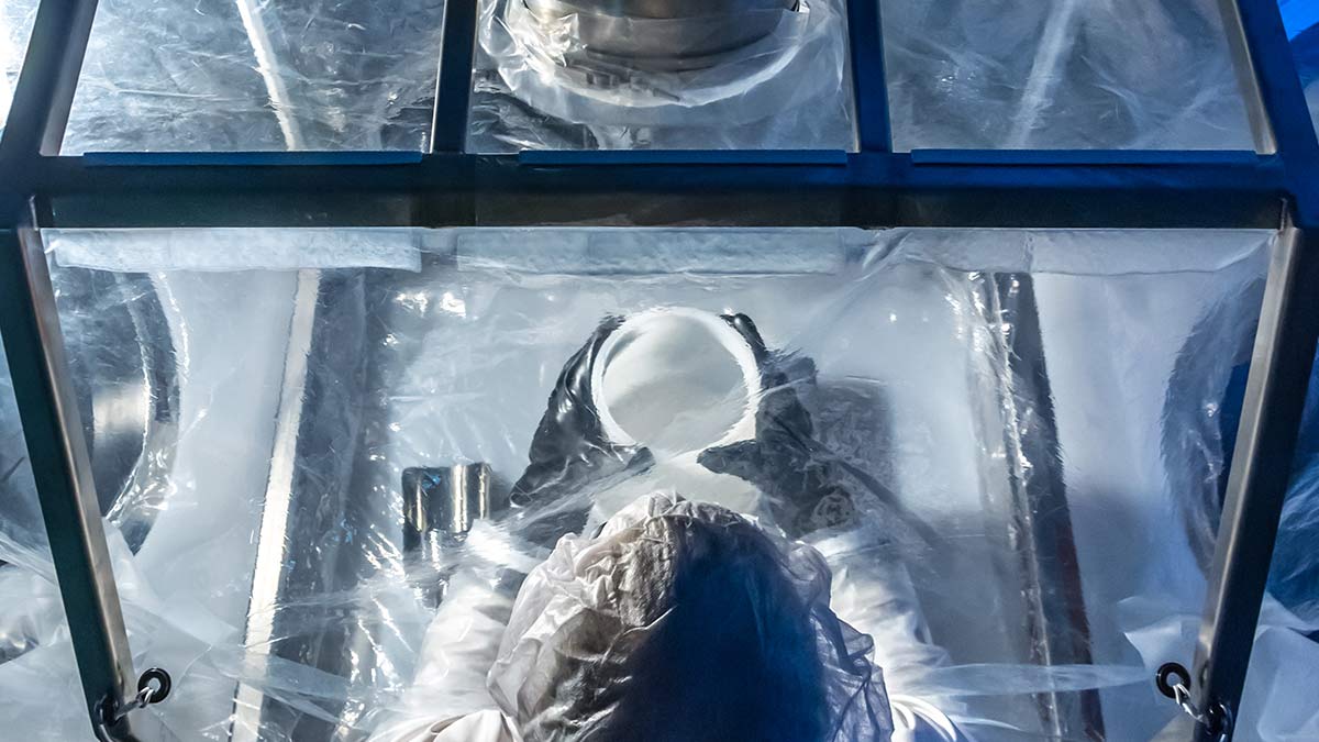 Aerial view of a biomanufacturing professional with personal protective equipment handling powders under a clear film
